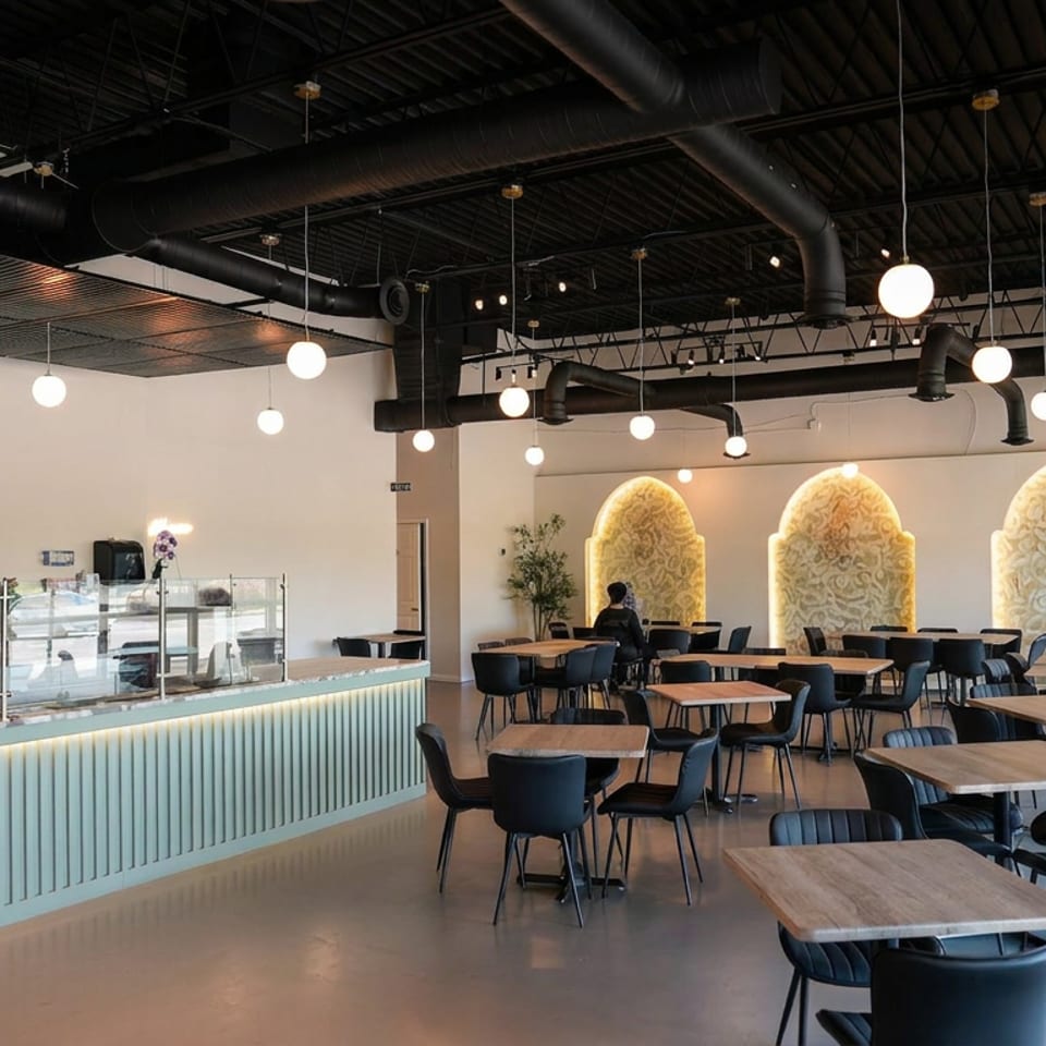 Modern Khana restaurant interior with wooden tables, dark chairs, glowing pendant lights, decorative wall arches, and a serving counter.