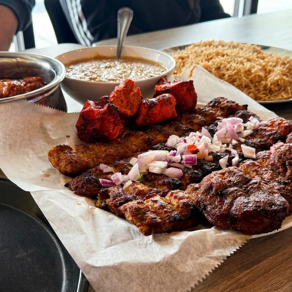 Assorted grilled meats, red chicken pieces, rice, curry, chopped onions, and Coca-Cola served on a restaurant table.