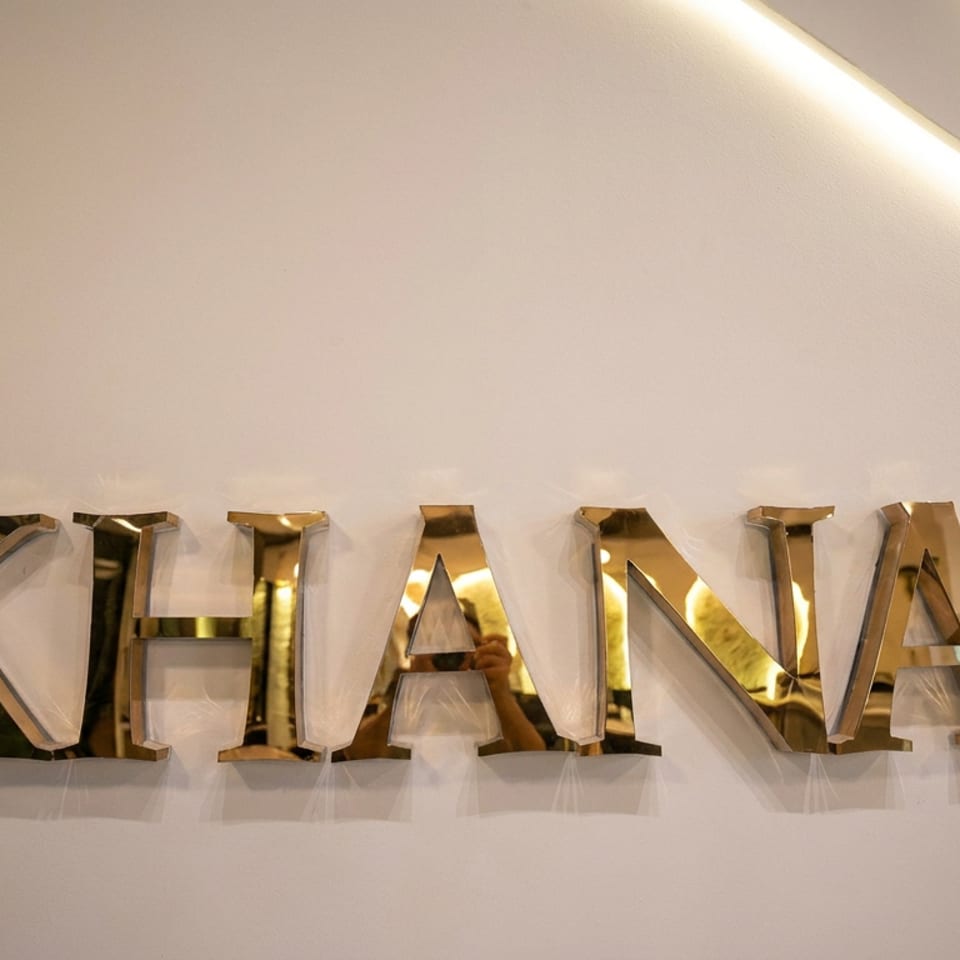 Gold K H A N A lettering mounted on a softly lit restaurant wall.