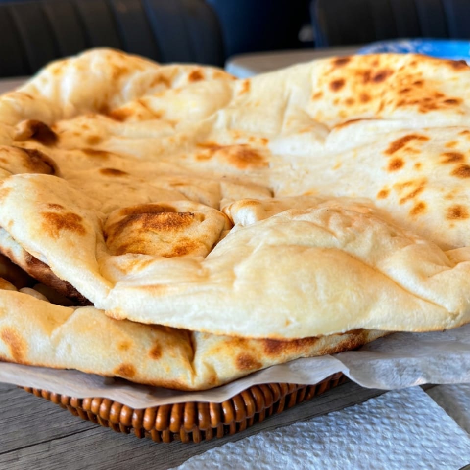 Stack of golden-brown flatbreads on parchment atop a woven basket on a restaurant table.